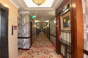 A hotel hallway with a patterned carpet, wooden doors, and a ceiling light fixture.