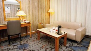Habitación de hotel con pared de madera, un escritorio con silla, un sofá, una mesa de centro y un espejo.