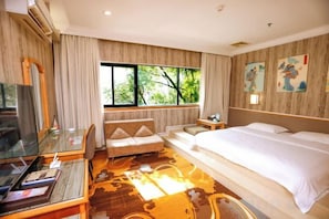 A hotel room with a bed, a sofa, a TV, and a window with a view of trees.