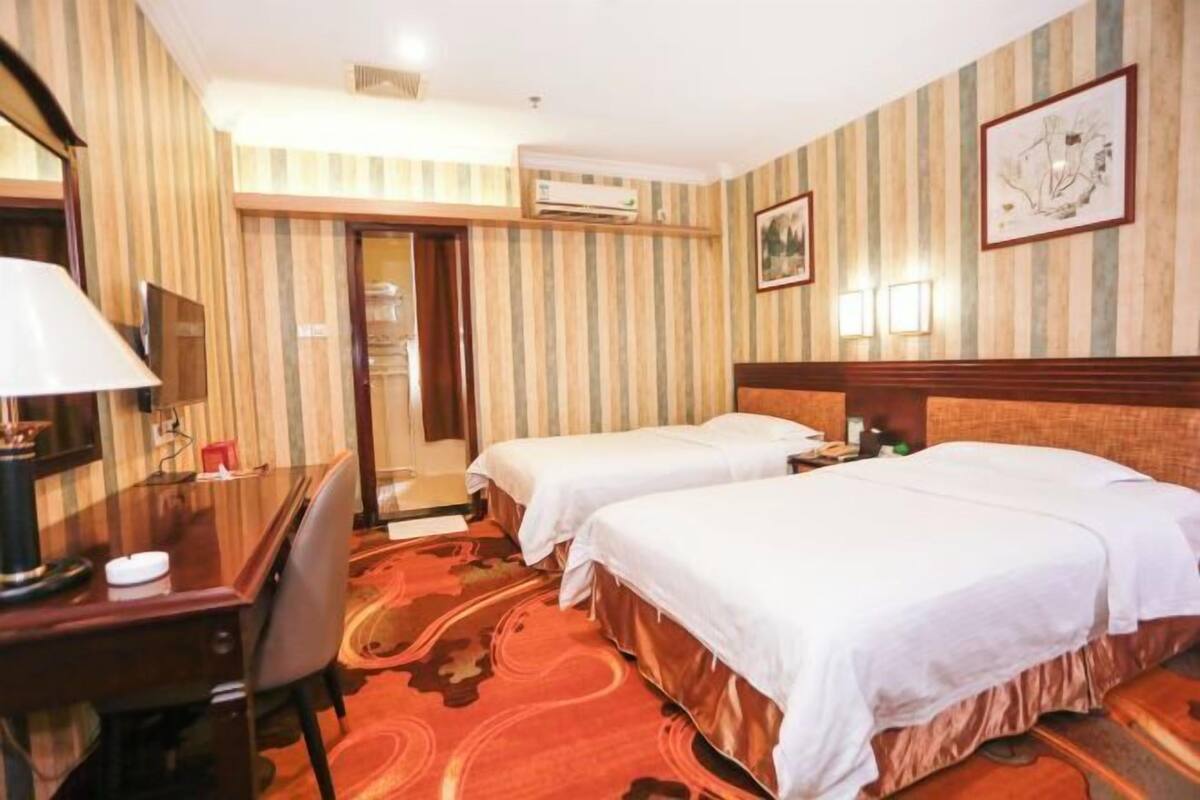 Hotelkamer met twee bedden, een bureau, een stoel, een airconditioning en een deur naar een badkamer.