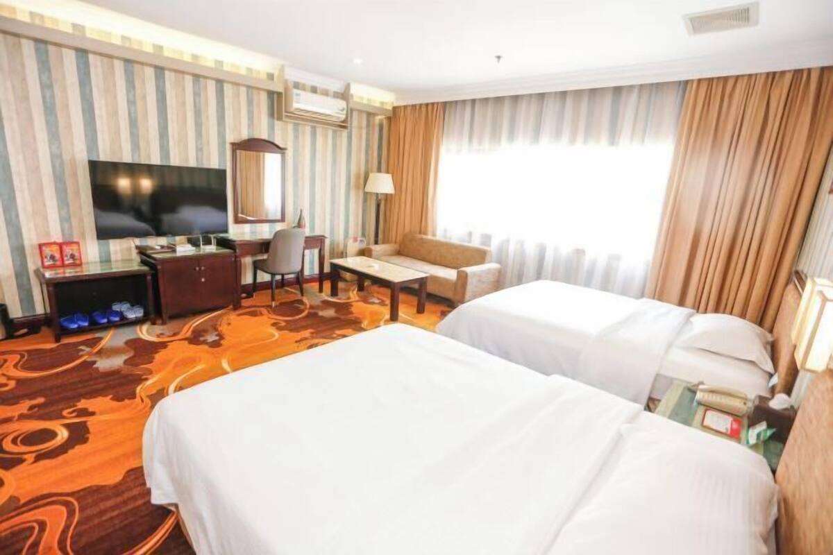 Een hotelkamer met twee bedden, een bureau, een stoel, een televisie en een groot raam met gordijnen.