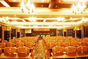 Un salón de conferencias con filas de sillas, mesas y un escenario al frente.