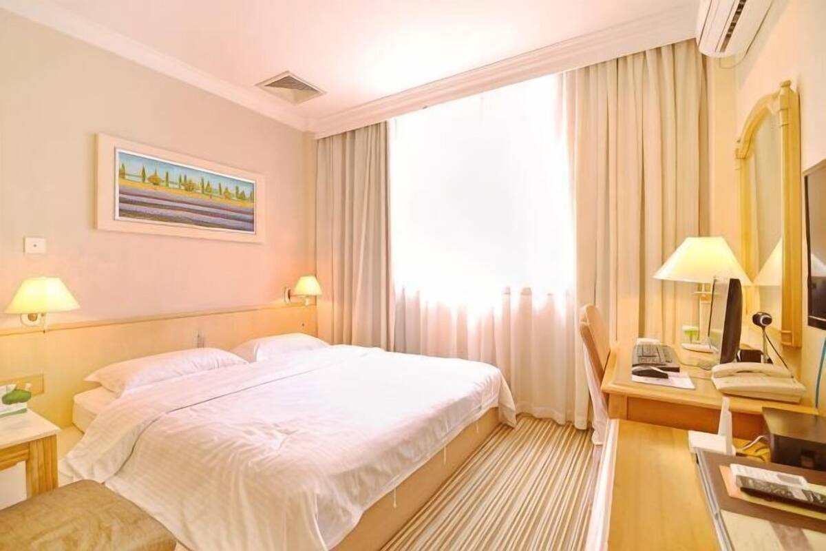 Een hotelkamer met een bed, twee nachtkastjes met lampen, een bureau met stoel, een spiegel en een raam met gordijnen.