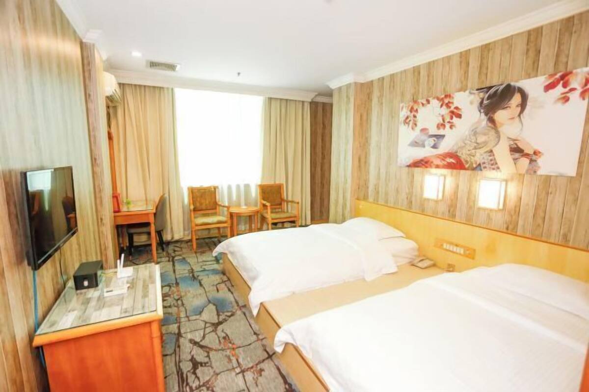 Een hotelkamer met twee bedden, een bureau met stoel, een flatscreen televisie en een groot raam met gordijnen.