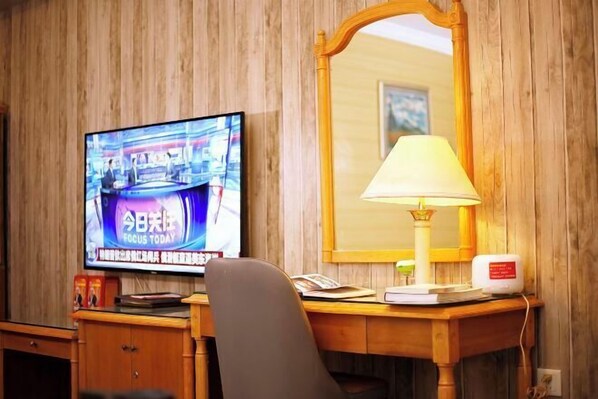 Une chambre d’hôtel avec un mur en bois, un téléviseur diffusant un programme d’information, un bureau avec une lampe et un miroir.