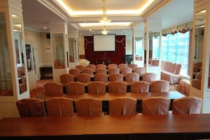Una sala de conferències amb una taula llarga i cadires, una pantalla de projector i un escenari.