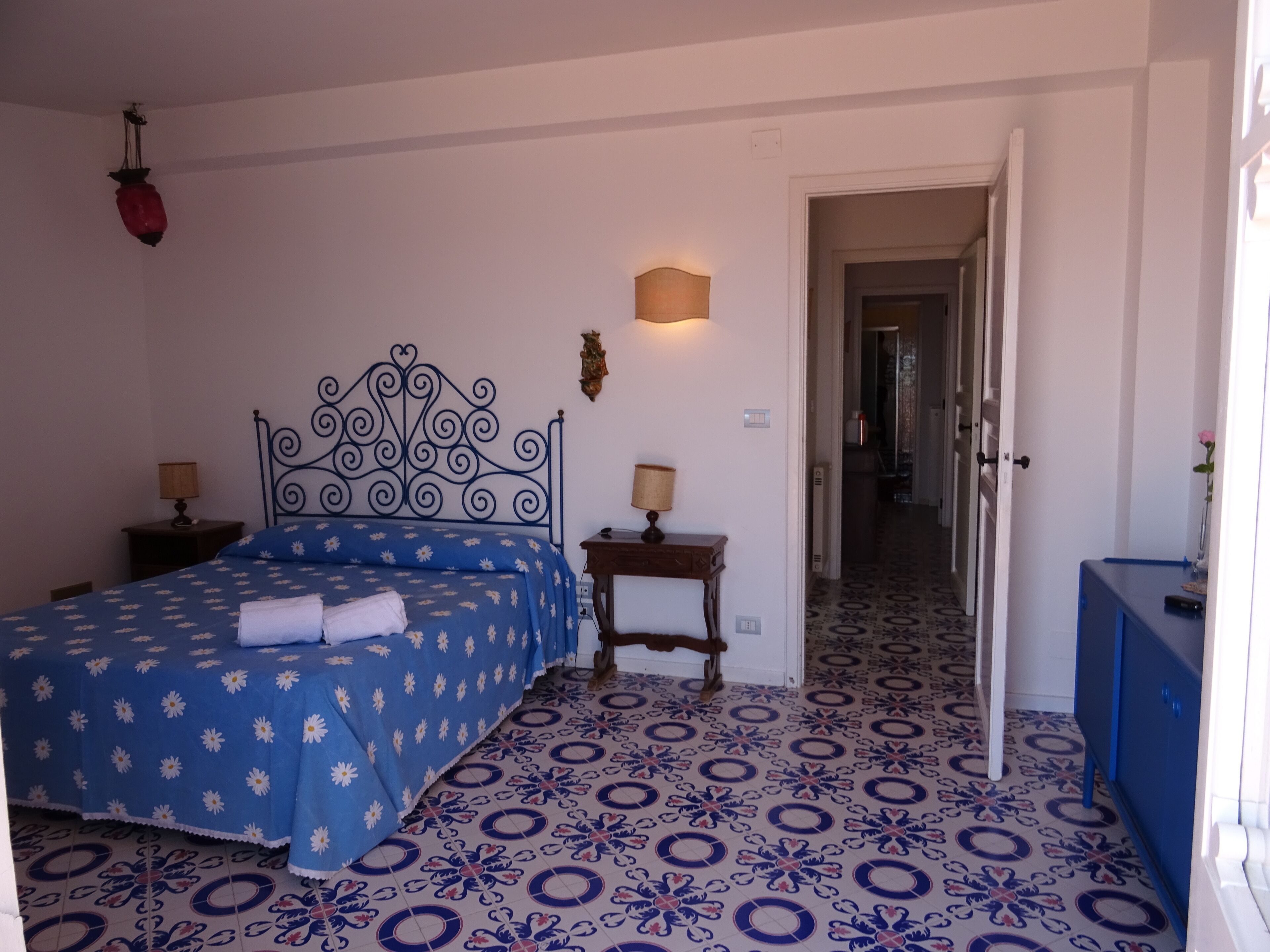 Ein Schlafzimmer mit einem gemusterten Boden, einem Bett mit blumigem, blauem Überwurf, zwei Nachttischlampen, einem Nachttisch und einer Kommode.