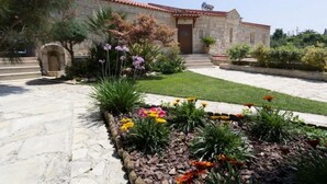 Ein Gebäude aus Stein mit rotem Ziegeldach, einem zentralen Eingang und einem Garten mit verschiedenen Pflanzen und Blumen.