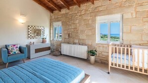 Ein Schlafzimmer mit Steinsandsteinwand, einem Bett, einem Babybett, einer Kommode und einem Fenster mit Aussicht.