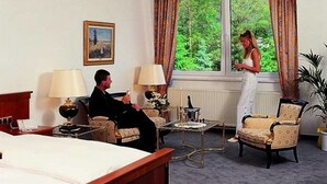 A hotel room with a bed, two armchairs, a coffee table, and a large window with curtains. - Hotel Restaurant Fasanerie (Marburg)