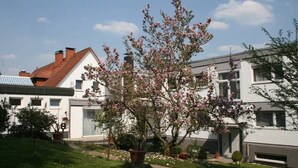 A residential area with two houses, one with a red roof and another with a white facade. There is a flowering tree in the foreground. - Hotel Restaurant Fasanerie (Marburg)