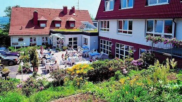 A hotel with a red roof, white walls, and a garden area with outdoor seating. - Hotel Restaurant Fasanerie (Marburg)