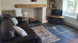 Ett mysigt vardagsrum med en lädersoffa, en tv, en öppen spis och ett stengolv.