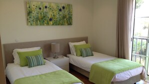 Ein Hotelzimmer mit zwei Einzelbetten, jeweils mit grüner Bettdecke und passenden Kissen, einem Nachttisch mit Lampe sowie einem großen abstrakten Gemälde an der Wand.