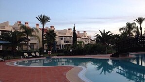 Ein Pool mit Liegestühlen, Palmen und mehrstöckigen Gebäuden im Hintergrund.