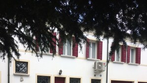 A building with a red door and windows with decorative iron grilles. There are potted plants and a gravel pathway in front. - historic dwelling (Mira)