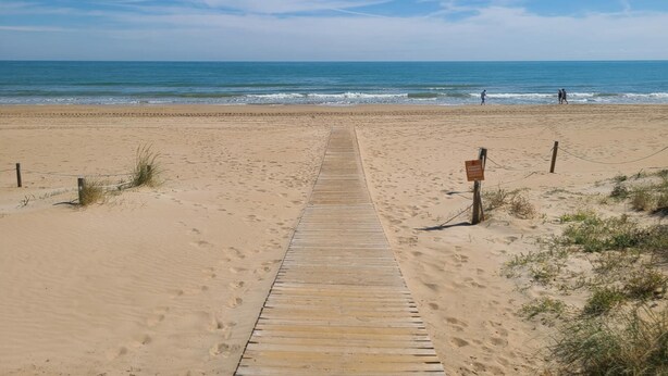 Een houten looppad dat naar een zandstrand leidt, met een heldere lucht.