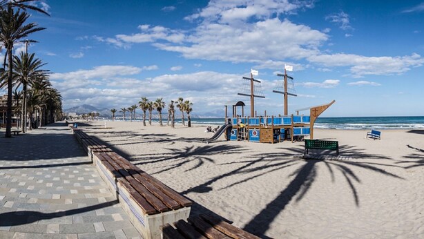 A beach with a wooden bench, palm trees, and a lifeguard tower.