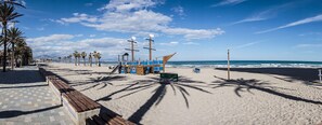 Una playa con un banco de madera, palmeras y una torre de salvavidas.