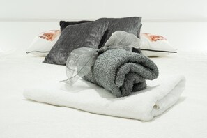 A neatly folded gray towel with a transparent bow on a white towel, placed on a bed with gray and white pillows. - Perfect place for family vacation (Dubrovnik)