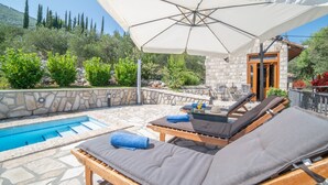 Un área junto a la piscina con sillones de descanso, una sombrilla grande y un muro de piedra.