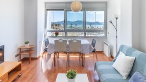 Una sala de estar moderna con comedor, ventanas amplias que dan a un paisaje costero y un sofá azul.