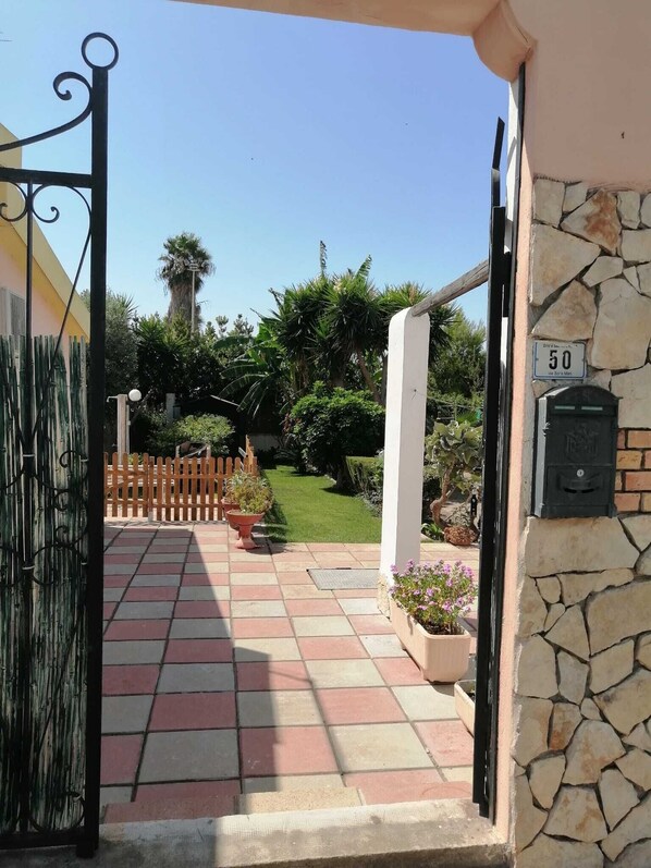 A paved entrance with a stone wall, a mailbox, and a wooden fence leading to a garden.