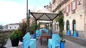 Un caffè all'aperto con sedie e tavoli blu, circondato da piante in vaso e una zona coperta.