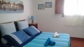Una camera da letto con un letto, cuscini, un comodino, una lampada e un quadro appeso al muro.