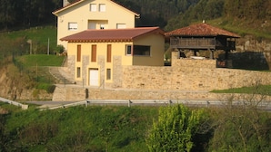 Une maison à deux étages avec une façade en pierre, un toit recouvert de tuiles rouges et une petite construction en bois sur le côté droit.