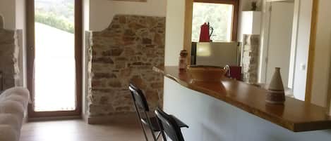 Una cocina con pared de piedra, encimera de madera, refrigerador, lavaplatos y ventana con vista a follaje.