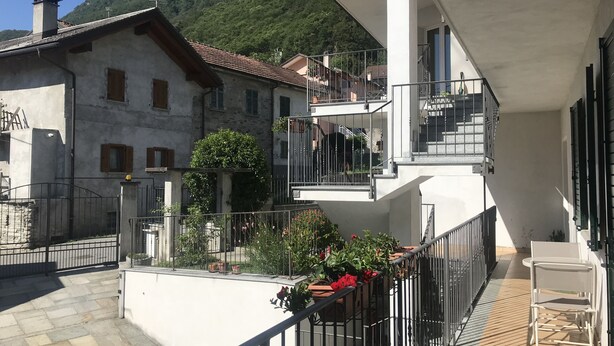 Un edificio de varios pisos con balcones, fachada de piedra y montañas al fondo.