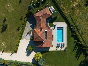 An aerial view of a house with a swimming pool, a covered patio, and a well-maintained lawn.