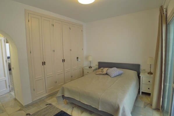 Quarto com cama, mesa de cabeceira, abajur e guarda-roupa.