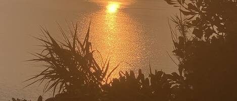 Solnedgang over et roligt hav med silhuetter af bjerge i baggrunden.