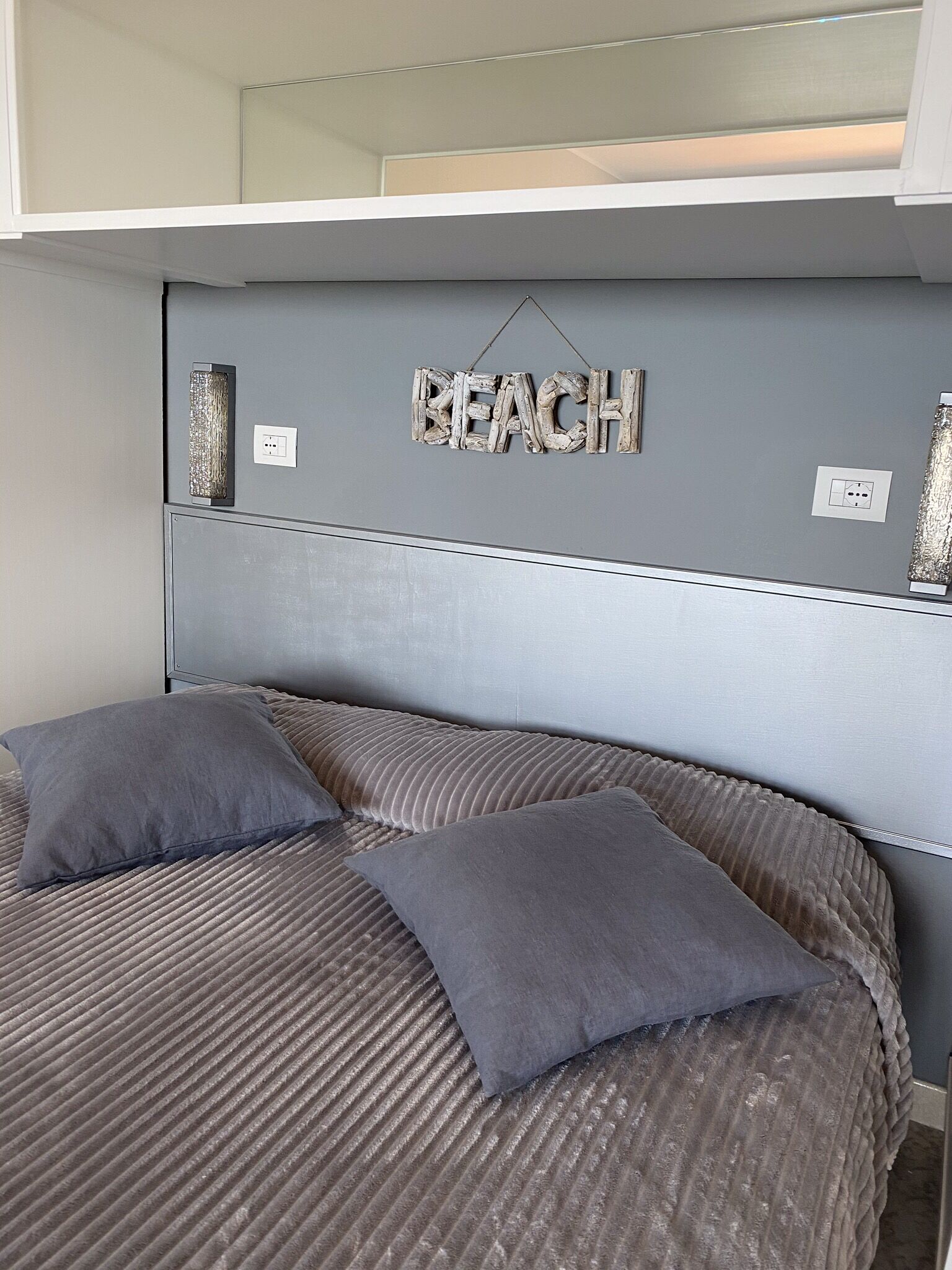 A bedroom with a bunk bed, a headboard with a 'BEACH' sign, and two pillows.