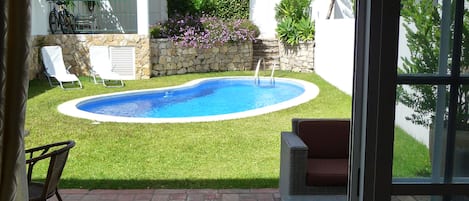 En trädgård med en pool, en uteplats med stolar och utsikt över ett bostadsområde.