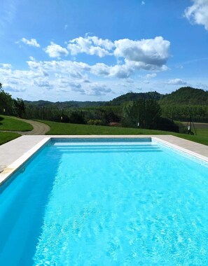 A rectangular swimming pool with clear blue water, surrounded by a paved deck.