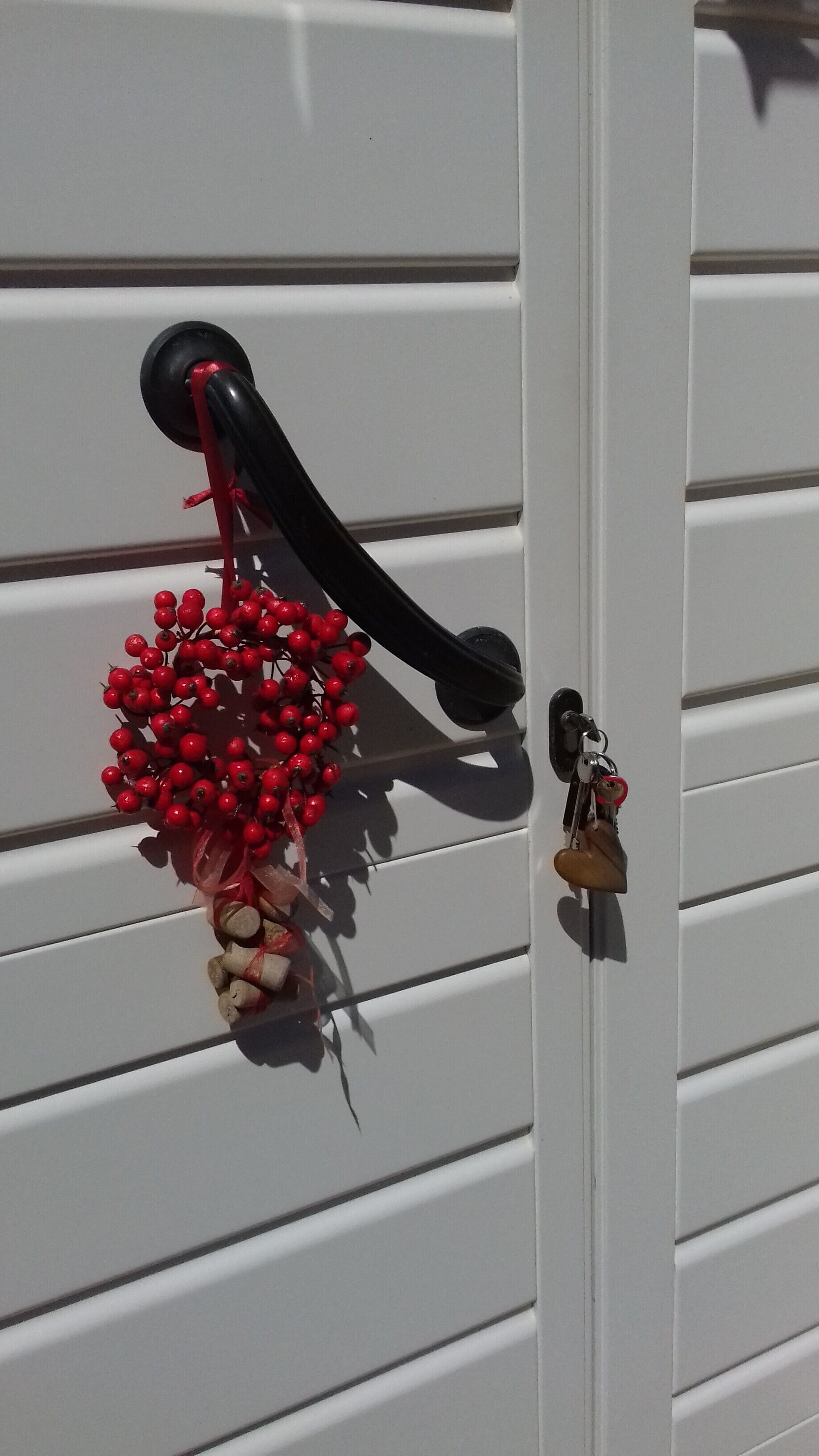 Un pomo de puerta con un llavero y una guirnalda decorativa de bayas rojas.
