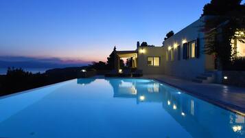 Ein moderner Infinity-Pool mit freiem Blick auf das Meer, ein gut beleuchteter Außenbereich und ein Gebäude mit markanter Architektur.