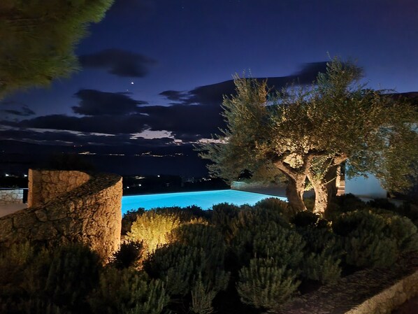 Vista nocturna de una piscina rodeada de árboles y un muro de piedra.
