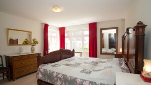 Une chambre à coucher avec un lit en bois, une commode, un miroir et une fenêtre ornée de rideaux rouges.