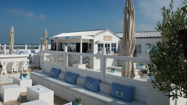 Un espace aménagé avec des sièges au bord de la plage, doté de mobilier blanc et de coussins bleus, offrant une vue sur la mer.