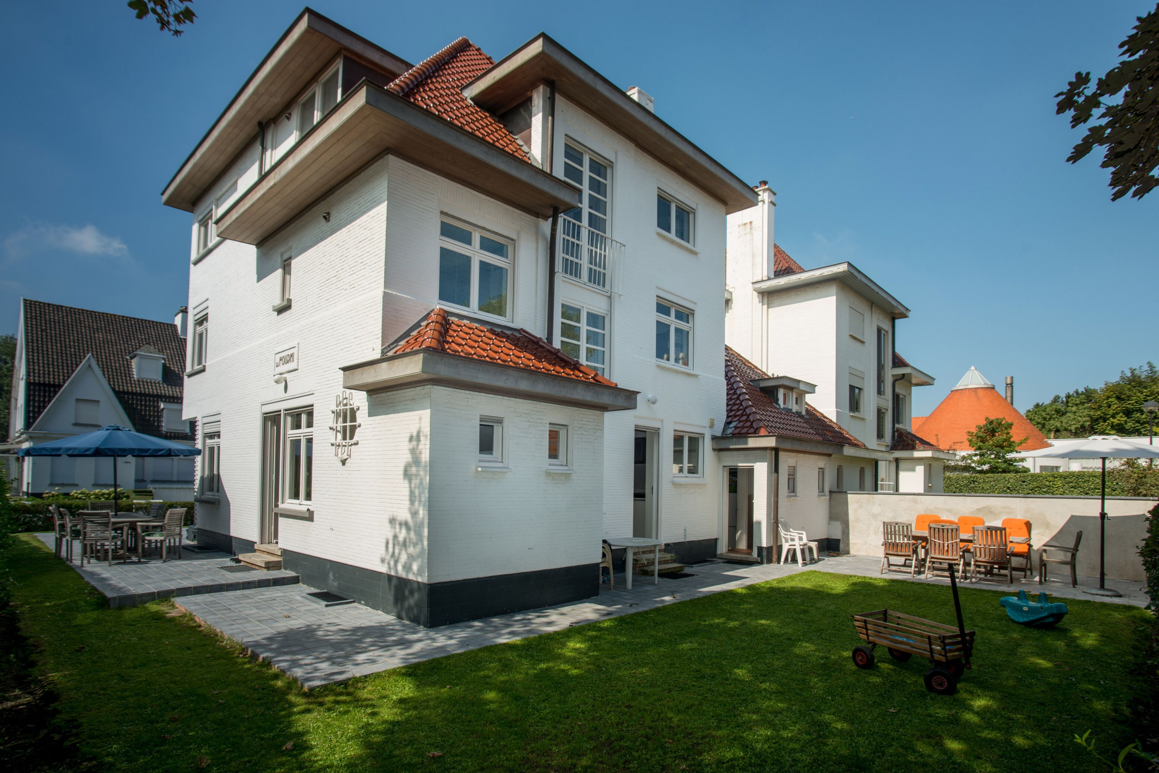 Een twee verdiepingen tellend huis met een patio, een kleine tuin en terrasmeubels.
