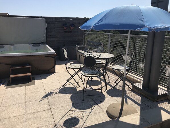 An outdoor patio area with a hot tub, a table with chairs, and a blue umbrella. - duplex penthouse apartment with large terrace near the beach of Sant Antoni (Sant Antoni de Calonge)