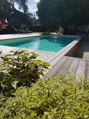 Una piscina con cubierta de madera, rodeada de abundante vegetación y un cielo despejado.