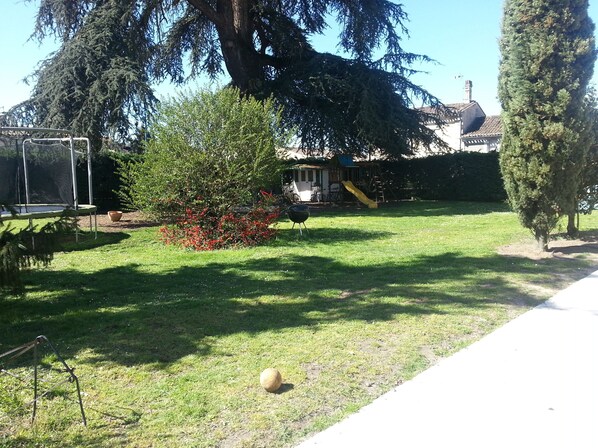 Un patio trasero con un trampolín, un árbol pequeño y un parque infantil.