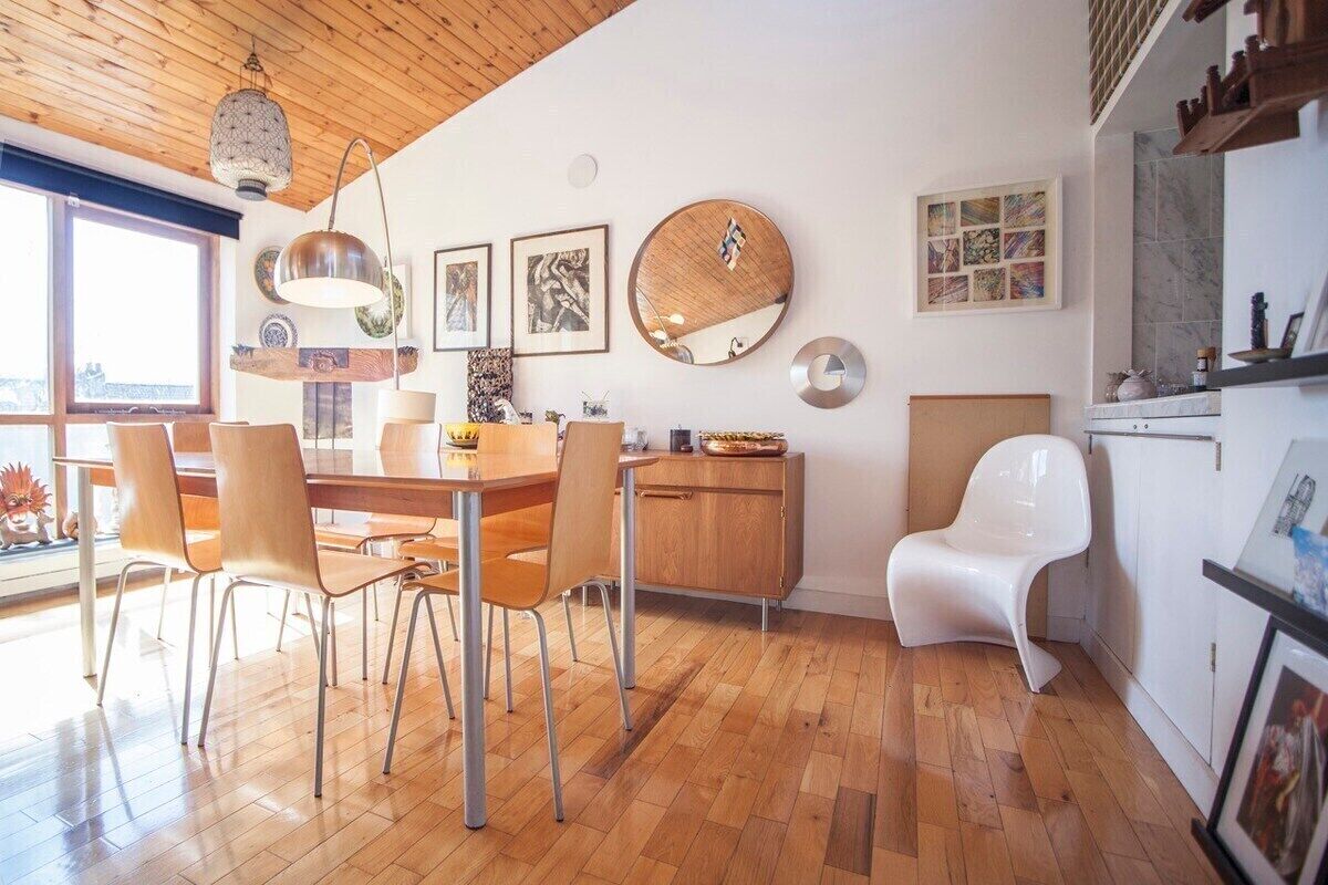 A modern kitchen with wooden flooring, a dining table with chairs, a white chair, and a cabinet.