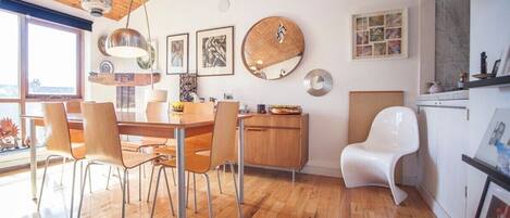 A modern kitchen with wooden flooring, a dining table with chairs, a white chair, and a cabinet.
