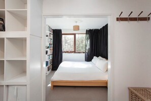 Een slaapkamer met een groot bed, een boekenkast en een raam met gordijnen.